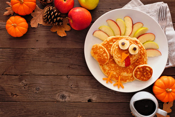 Cute Thanksgiving turkey pancakes. Top view corner border against a rustic wood background with...