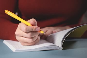 Woman is writing by a ballpen in her notebook close up background.