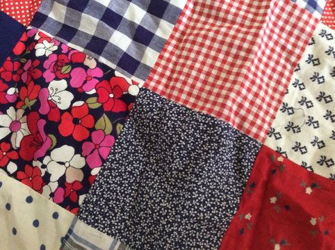 Close up of retro vintage material quilt handmade in 1970 design with cotton cloth check florals and reds yellow black white in square shapes sewn together 