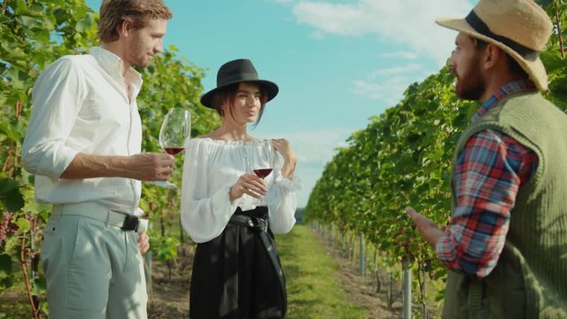 Romantic young fashion couple tasting pinot listening to proud farmer guiding interesting wine tour in vineyard agriculture field.