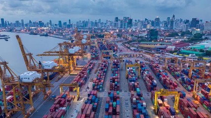 Aerial drone hyper lapse over industrial import  export port of Thailand in Bangkok with many rows and stacks of container and big container loader ship vessel at night.