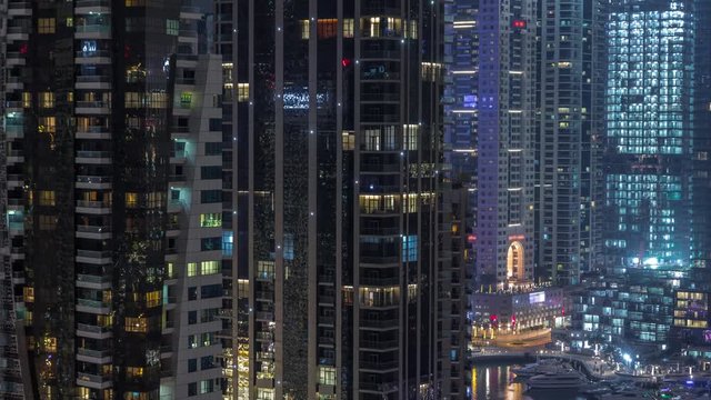 Aerial view of Dubai Marina residential and office skyscrapers with lights in windows and waterfront night timelapse. Floating boats and yachts
