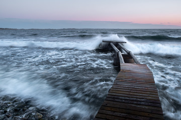 Waves crash over a broken pier in the ocean