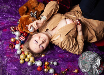 Top view of a young woman lying on the floor surrounded with nicely christmas toys balls and wrapped present