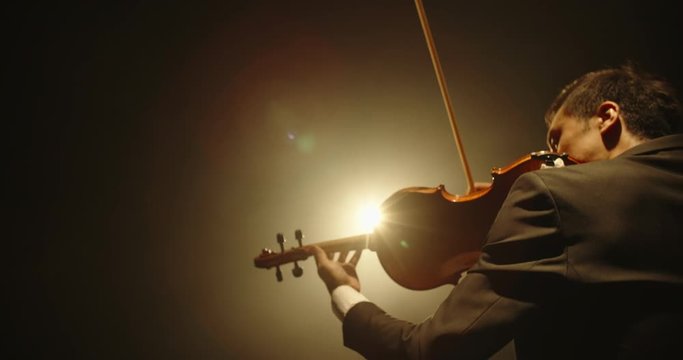 Male violin player having a solo on stage. Professional musician wearing tux is spotted by light on black background 4k footage