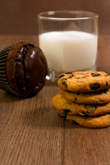 Chocolate muffin, a glass with milk and cookies on a wooden table.