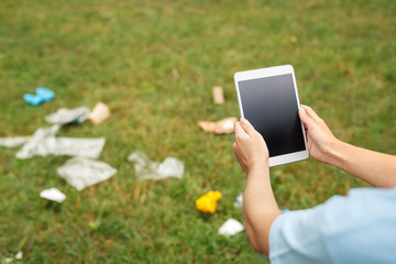 Leisure Outdoors. Young girl sitting in park taking photo of litter on digital tablet close-up