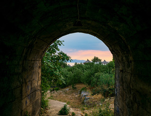 Fototapeta na wymiar Blick durch einen Tunnel auf einen Sonnenuntergang an der Adriaküste mit Sonnenliege und Sonnenschirm 
