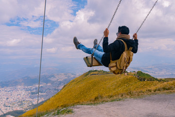 man on swing looking at the city from the mountain