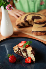 Homemade chocolate zebra cake with strawberries on dark blue plate on wooden table