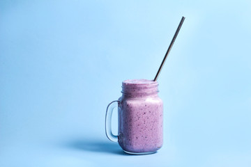 Blueberry smoothie drink in mason jar glass with reusable stainless steel straw on blue background