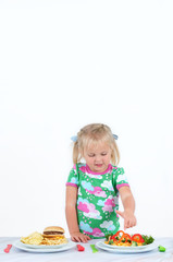 Little girl is choosing between junk and healthy dish. Vegetables full of vitamins are essential for the kid's menu.