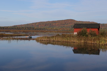 Man paddling a canoe from a red boat shed on Eel River, New Brunswick, Canada, in early morning on an autumn day.