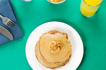 Pancakes with peanut butter on top. Served with some fruits and orange juice on the side