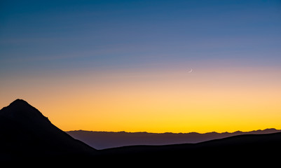 USA, Nevada, Nye County, Death Valley National Park. A High contrast blue orage yellow sunset background with fingernail moon that looks like another planet from a sci fi flick.