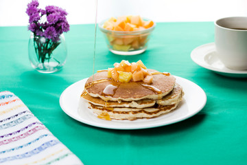 Oatmeal pancakes with tropical fruits on top and honey dripping. Served with coffee.