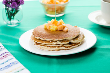 Oatmeal pancakes with tropical fruits on top and honey dripping. Served with coffee.