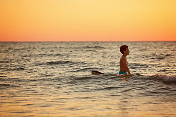 Confident boy carrying surfboard while standing at seaside in sunset