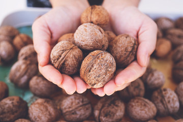 Detail of young woman's hands, holding a handful of organic walnuts. Selective focus