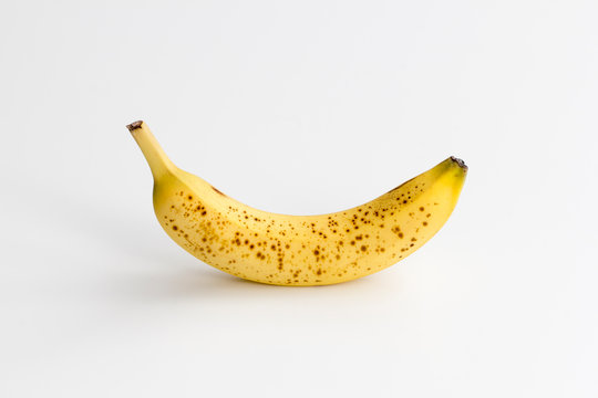Single ripe banana with brown spots centered and isolated on a white background.