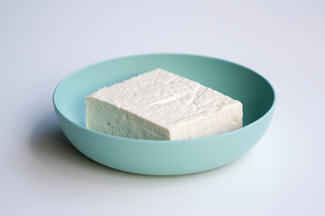 Closeup of fresh firm tofu in a bowl with selective focus isolated on a white background.