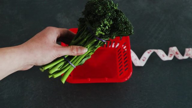 dieting concept, hand placing broccolini next to groceries shopping basket with measuring tape