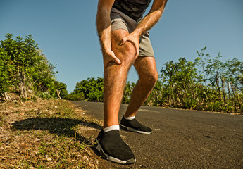 close up hands and legs of sport man injured touching his knee in pain suffering physical problem or some injury during running workout outdoors in health care concept