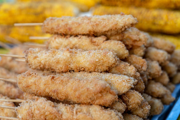 Skewers with fried chicken wings in batter for sell in street food market, Thailand, closeup