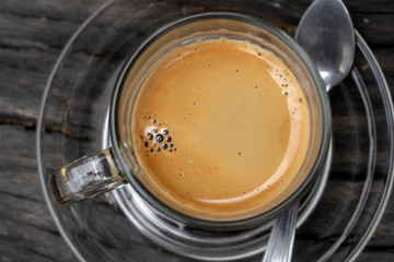 Glass cup of hot espresso coffee on wood board, closeup, top view