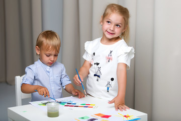 Brother and sister, girl and boy paint with watercolors at the t