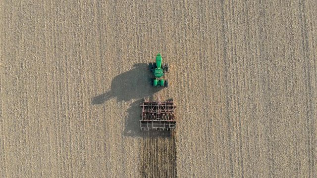 Top-Down Drone Footage Over a Green Tractor Plowing a Farmer's Field on a Warm Summer Day in Ontario.