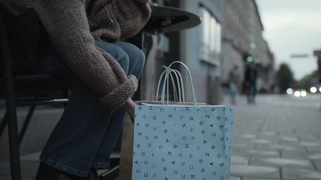 A woman sitting down and picking up one of her shopping bags.