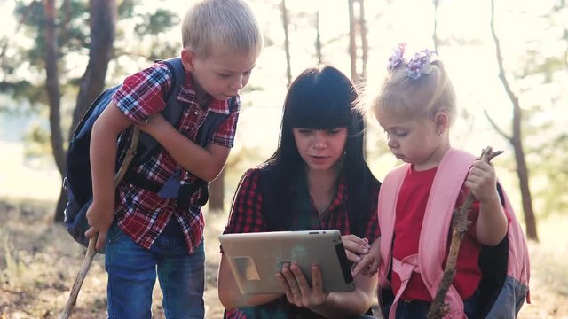 happy family little boy and girl scout navigation tourists teamwork slow motion video concept. mom son and daughter hiking in the forest looking for a way on a digital tablet. group of lifestyle