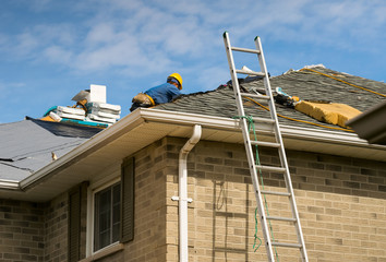 Roof worker installing new shingles on a roof of a house