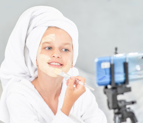 Young girl in towel on her head  filming the video for her followers about clay facial mask . Kids blogger concept