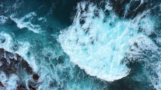 Top down abstract aerial view of ocean waves crashing on rocky coastline