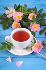Cup of hot tea and wild rose flower on blue boards