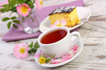 Obraz na płótnie Canvas Cup of tea with cheesecake and wild rose flower