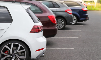 Closeup of rear, back side of white car with  other cars parking in outdoor parking area.