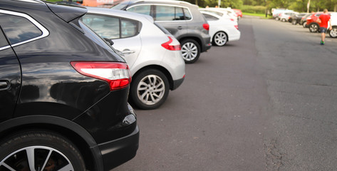 Closeup of rear, back side of black car with  other cars parking in outdoor parking area.