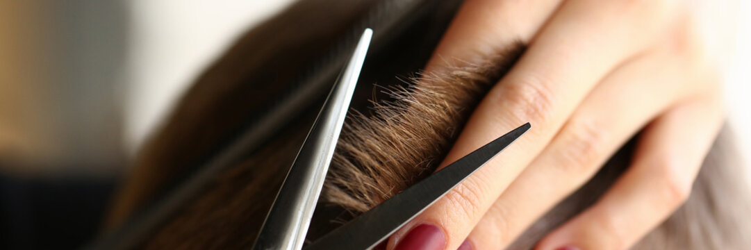 Female hand hold hair scissors aganist hairdresser salon background