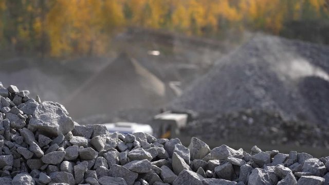 A truck filled with gravel leaves the loading point. Industrial background - crusher stone crushing machine at the quarry of a mining and processing plant for crushed stone, sand and gravel.