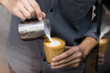 Close-up of male barista hand holding and pouring hot milk for prepare latte art on piccolo latte...
