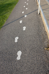 White footstep symbol painted on the asphalt ground floor to guide the tourist for the position