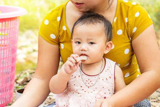 Little Asian baby girl sitting on her mom's legs who eating a piece of grilled meat