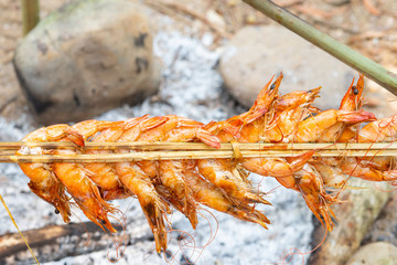 Shrimps attaching on stick grilling over stove