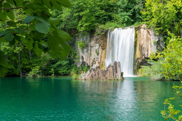 Fototapeta na wymiar Crystal clear, pure water rushing down mossy rocks into a beautiful azure colored lake at the Plitvice Lakes National Park in Croatia