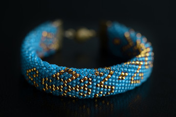 Fototapeta premium Beaded bracelet blue color with golden pattern on a dark background close up