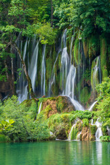 Crystal clear, pure water rushing down mossy rocks into a beautiful azure colored lake at the Plitvice Lakes National Park, Plitvička Jezera, Croatia