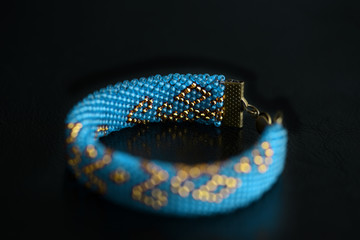 Beaded bracelet blue color with golden pattern on a dark background close up